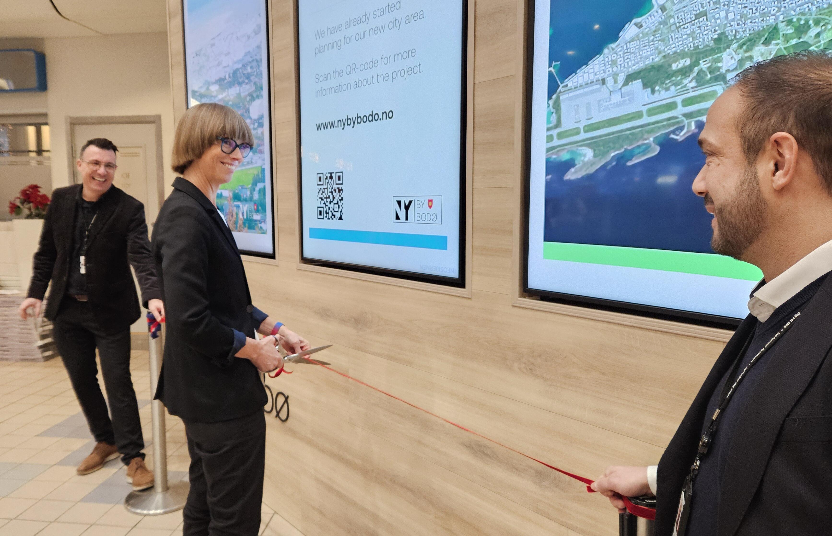 Bildet viser varaordfører Ida Gudding Johnsen som klipper snora i anledning den offisielle åpningen av en ny informasjonsvegg på Bodø lufthavn.  